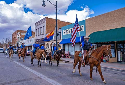 Members of the Clear Creek Cowboys ride through Winslow with US, Arizona and Post Office flags. Pictured are (right to left) David Ramos, Tammy Gray, Deena Clark, Leigh Barthen and Enrique Pacheco followed by the rest of the cowboys participating in the ride.