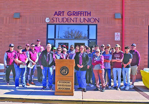 Just a few weeks after the City of Winslow unveiled a monument in honor of his enduring legacy, Coach Art Griffith (left of podium), a revered figure at Winslow High School, stands before the newly renamed Art Griffith Student Union. This event draws a supportive crowd that includes friends, community members, WHS baseball players, and the school's dedicated staff. This gathering around Coach Griffith celebrates his monumental contributions and marks a deeply historic occasion that resonates across both the school and the entire Winslow community.