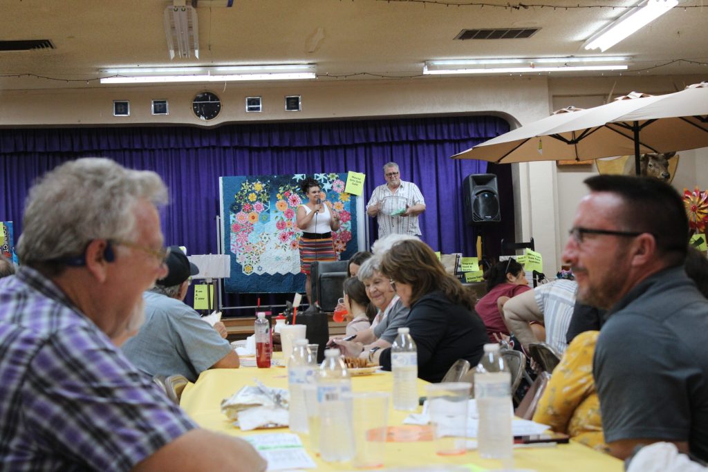Locals share laughs together while Darcey McKee and Bob Hall (on the stage) auction off items for the Chamber of Commerce’s annual fundraiser.