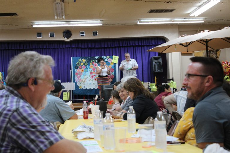 Locals share laughs together while Darcey McKee and Bob Hall (on the stage) auction off items for the Chamber of Commerce’s annual fundraiser.