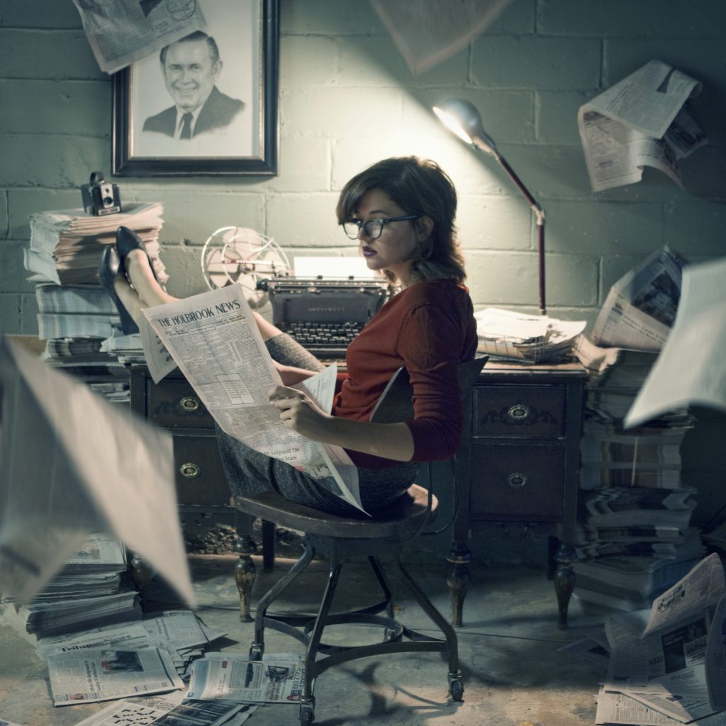 This photo was taken in 2015 by local artist and The Tribune reporter Talaina Kor. Kor, who is featured in the photo, included a sketch of former owner and publisher Paul Barger on the wall and objects used throughout the years in publishing The Tribune. The newspaper held by Kor features the first edition printed by The Holbrook News melded with the current edition in 2015.