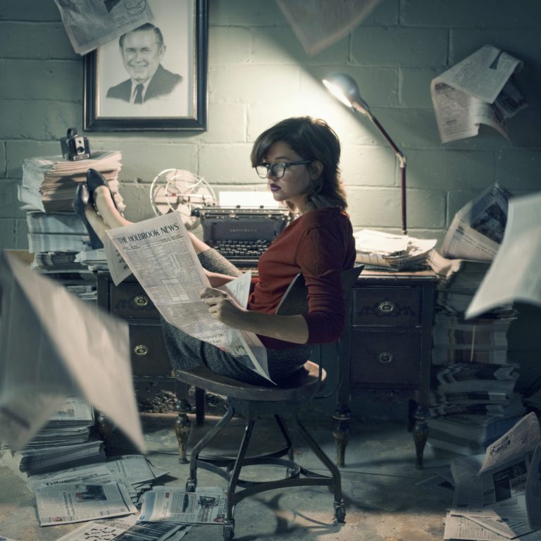 This photo was taken in 2015 by local artist and The Tribune reporter Talaina Kor. Kor, who is featured in the photo, included a sketch of former owner and publisher Paul Barger on the wall and objects used throughout the years in publishing The Tribune. The newspaper held by Kor features the first edition printed by The Holbrook News melded with the current edition in 2015.
