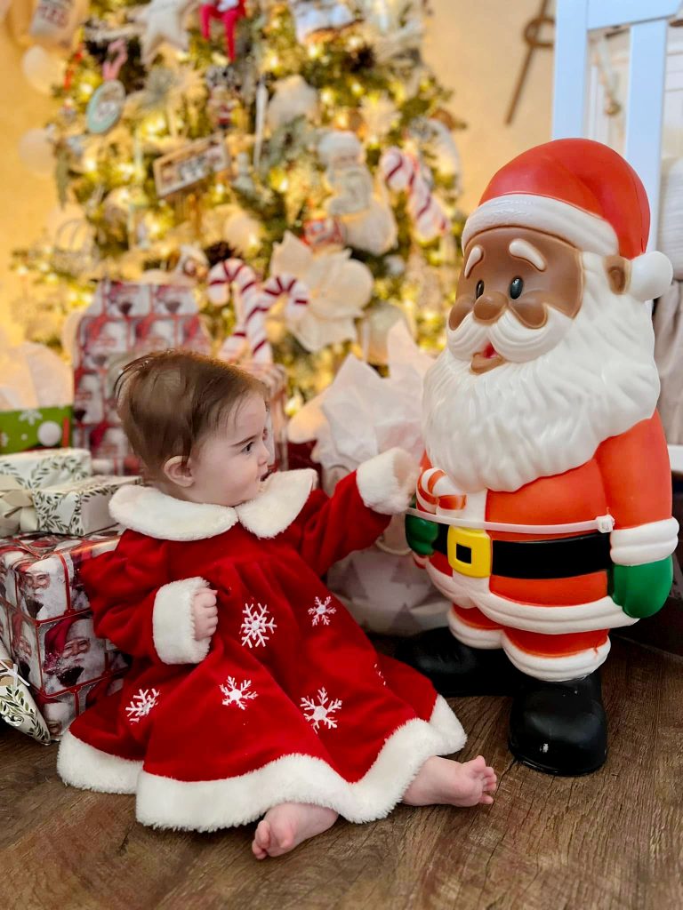 Hallie Fugatt welcomes Winslow’s Traveling Santa to sit with her at the Christmas tree. This plastic Santa carries with it the love and good cheer of friends and neighbors as it travels from home to home throughout the holiday season.