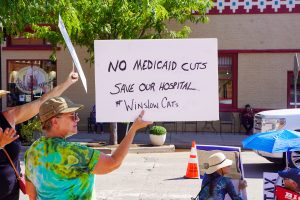Teri Parsons holds a sign protesting Medicaid cuts along with approximately two dozen others at Route 66 Plaza in Winslow as residents marked the anniversary of Congressman John Lewis’s death with a call to make “Good Trouble.” The event featured speakers from the local Democratic Party and a giant banner reading “Save Our Democracy.”