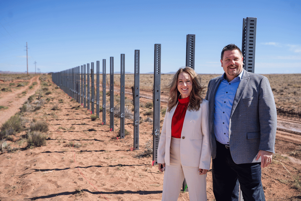 Cindy Baier, left, and Gordon Baier stand next to a row of poles installed in the ground between two ranches near Holbrook that are expected to later be fitted with double-sided solar panels as part of GoSolar.US’s solar fence project.