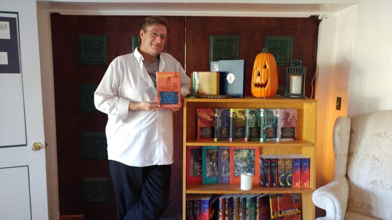 Photo by Naomi Hatch - James Owen, a Taylor writer and illustrator, shows off his newest book, The Dragon Knight. The bookcase displays many of the books he has written throughout the years.