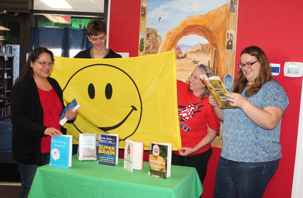 Photo by Linda KorApril is Happy Holbrook Month, when residents are reminded to share a smile, a kind word and take positive action. Here (left to right) library assistant Carmen, Josh Fisher, Librarian Wendy Skevington and library assistant Emily Whitehorn work together to set up library books and signs for the upcoming month. The city will once again be holding a contest to determine the happiest person, happiest business and brightest smile throughout the month.