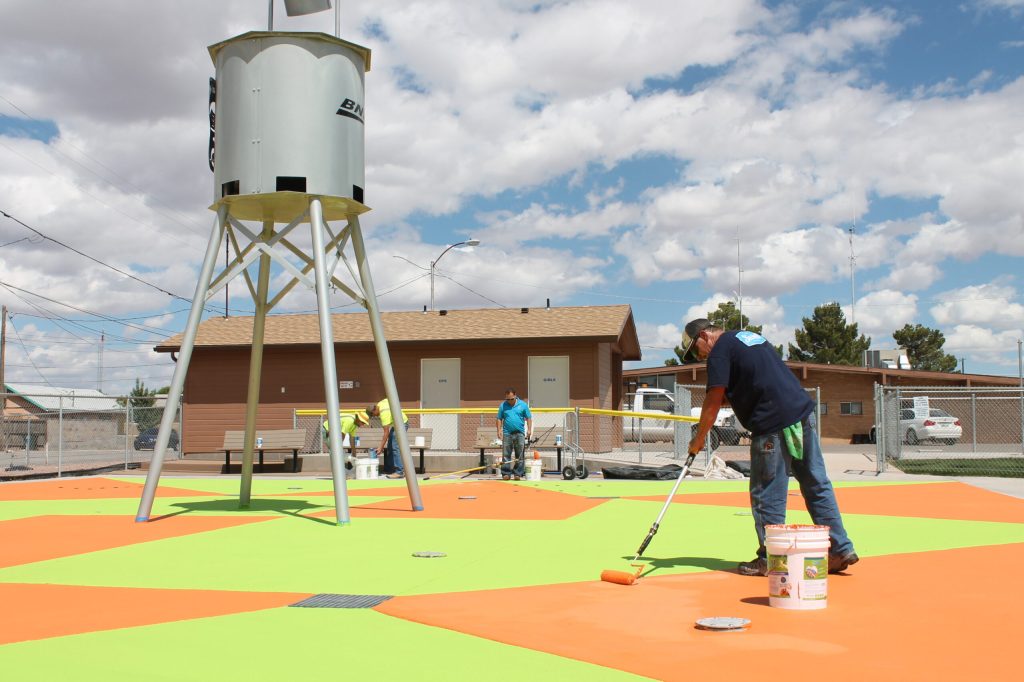Photo by Linda KorThe City of Holbrook is getting its recreational facilities ready for some summer fun, including a new paint job and sealant for the splash pad. Facilities and Maintenance Head Tim Kelley (front) puts on a second coat of bright orange paint to go with the lime green, a combination of what he called “kid-friendly colors.” Also lending a hand on the project are (left to right) City Manager Randy Sullivan, city employee Michael Young and Mike Stockley of Commercial Pool Repair. The splash pad will be open by the end of this week.