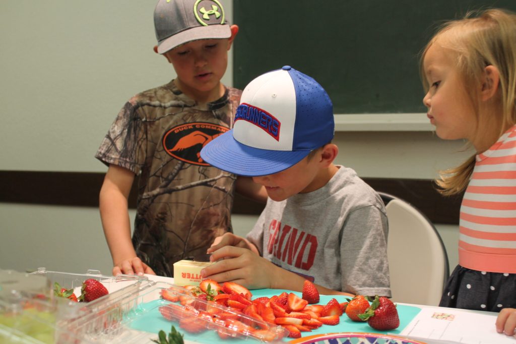 Photo by Linda KorTildyn (left) and Tayla Larson (right) look on as their brother Ty shows them how to cut butter according to a recipe for fruit pizza they were learning to make. They and others enjoyed a kids’ cooking class hosted by the City of Holbrook and taught by Kellie Spangler as part of the city’s summer recreation program. For information on activities offered this summer, call city hall at 524-6225.