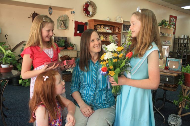 Photo by Linda KorThis Sunday, May 13, is Mother’s Day and it’s all about showing mom how much she is loved and recognizing how much she gives of herself when raising her family. The joy of motherhood and the love it brings is apparent here as Carrie Burgess of Holbrook enjoys gifts selected by her daughters (left to right) Sarah, Naomi and Abigail at Pat’s House of Originals.
