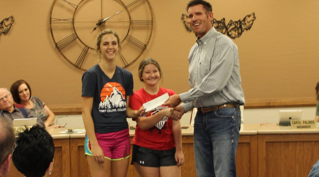 Photo by Toni GibbonsSnowflake High School students Chloe Lyman (left) and Lanee Penrod (center) from the girls’ volleyball club accepted a $300 check for their team from Bob Flake (right) of the Snowflake Rodeo Committee at the Snowflake School District meeting on Aug. 9.