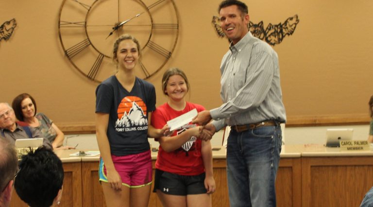 Photo by Toni GibbonsSnowflake High School students Chloe Lyman (left) and Lanee Penrod (center) from the girls’ volleyball club accepted a $300 check for their team from Bob Flake (right) of the Snowflake Rodeo Committee at the Snowflake School District meeting on Aug. 9.