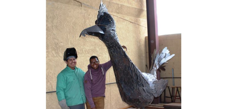 Photo by Toni GibbonsHolbrook High School senior Kamal Yazzie (right) stands with classmate Marco Luna (left) next to the famed roadrunner, which has been an ongoing project in HHS Career and Technology welding program for the last five years. Yazzie dreams of being able to finish the nearly 150 feathers left to place on the bird before he graduates.