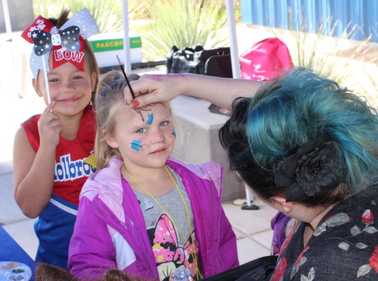 Photo by Toni GibbonsStacy Ashcroft, cosmetology instructor at NPC’s Little Colorado Campus in Winslow, paints the face of 5-year-old Emalie McCollam, from Holbrook, while her 8-year-old sister, Erin McCollam, stands behind her. The two sisters came to the event with their mom, Sheri McCollum.