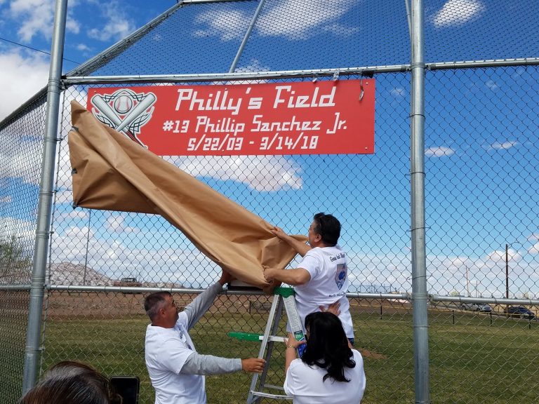 Photo by L. ParsonsPhilip Sanchez Sr. (center) unveiled the sign renaming the South Side baseball field in honor of his son, Philly who succumbed to an illness last year. Philly’s mother Denise Sanchez (right) and his uncle, David Sanchez (left) looked on. The field, located at Sacred Heart Park on Jefferson Street, was dedicated as Philly’s Field with over 100 people in attendance. Winslow City Manager John Barkley spoke to the crowd and expressed his respect for the family and for the legacy of Philly.