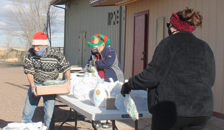 Photo by China CassidyOn Saturday, Dec. 19, members of the Holbrook Elks Lodge handed out bags of toys, food boxes and gift cards that can be used to help purchase shoes and coats from Walmart to 50 families for the holidays. Pictured are Beverly Goodnight (center) who handed out hot dogs to families waiting in line while Phil Cobb (left) handed out the supplies along with Kassandra Grabowski (right).