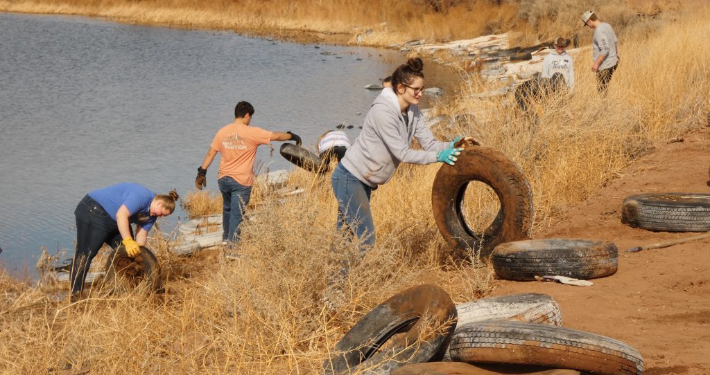 Photo by Michael O’DellLDS missionary Jessica Jensen (center) rolled up a tire out of the clay soil as one of the 10 missionary volunteers that showed up to remove old tires wedged along the banks of the newly named Blue Heron Lake at the Hidden Cove Golf Course.