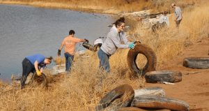 Photo by Michael O’DellLDS missionary Jessica Jensen (center) rolled up a tire out of the clay soil as one of the 10 missionary volunteers that showed up to remove old tires wedged along the banks of the newly named Blue Heron Lake at the Hidden Cove Golf Course.