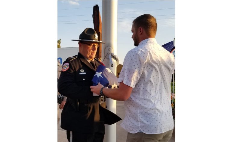 Photo by L. ParsonsThe community of Winslow came together, approximately 300 strong to memorialize the 20-year anniversary of the Sept. 11 attacks. Here, Casey Hancock (right) receives a flag from Sheriff’s deputy Ron Chisolm. Hancock is the grandson of the late Dale Hancock who was instrumental in bringing pieces of the Twin Towers to the Winslow Memorial Garden on Third Street.