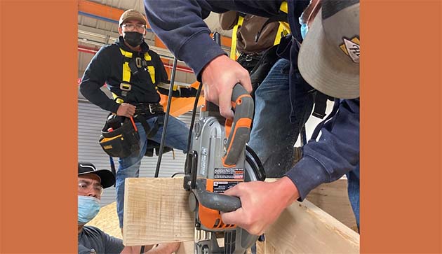 Photo courtesy of Northland Pioneer CollegeNPC student David Milligan cuts a roof ridge beam to prepare for the installation of a fascia. Fellow students Cayden Begaye and Jesus Cisneros observe.