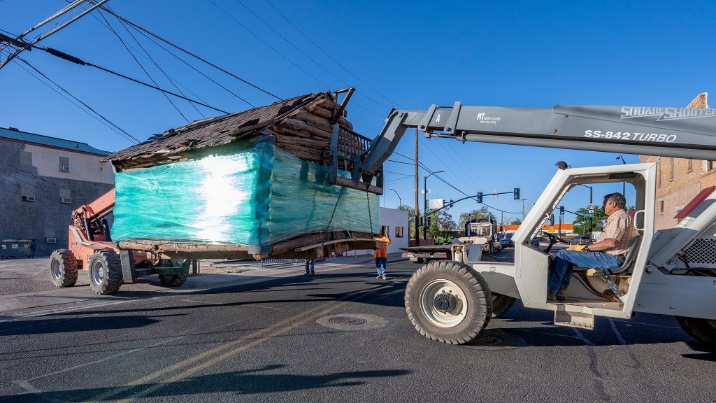 Photo by Jim Buckley Winslow’s historic “Birthplace Cabin” made its way to its new permanent home last week. Here, Winslow’s Gene Hancock helps lift the structure from the back of a truck. The cabin was moved from Brigham City to a park on Williamson Avenue in Winslow, a space closer to its original location when it was built in the late 1860’s. The cabin is considered the first permanent residence built in Winslow and housed several prominent citizens over the years. The Winslow Historic Preservation Commission facilitated the move.