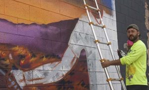 Photo by L. ParsonsMuralist Isaac Caruso is shown here completing a piece in Winslow on the corner of Kinsley Avenue and Third Street. The piece is part of an illustration project for his 43-page children’s book “Sam and Sarah,” which he plans to illustrate entirely with street art across the state.