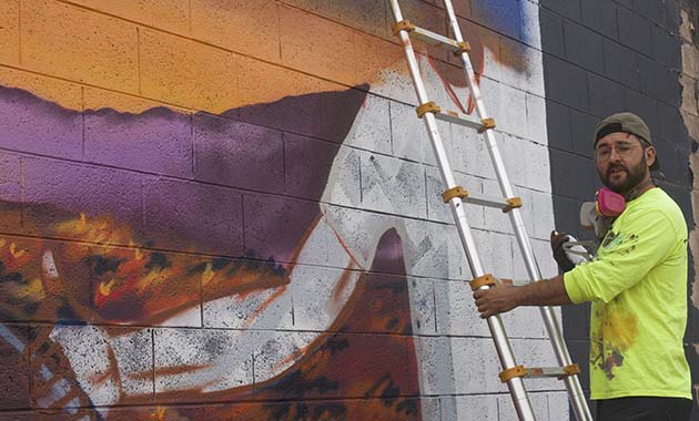 Photo by L. ParsonsMuralist Isaac Caruso is shown here completing a piece in Winslow on the corner of Kinsley Avenue and Third Street. The piece is part of an illustration project for his 43-page children’s book “Sam and Sarah,” which he plans to illustrate entirely with street art across the state.