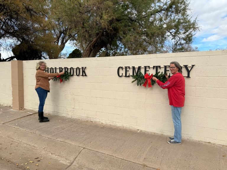 Photo by Kathleen SmithMembers of the Holbrook community donated their time and money to add a touch of holiday décor to the cemetery walls last week. Robin Gonzales (left) and Councilmember Teri Tafoya (right) placed wreaths along the walls, with bows donated by Lois and Gerald Hancock.